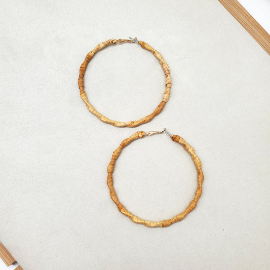 Two gold hoop earrings wrapped in cedar bark on a light gray surface.