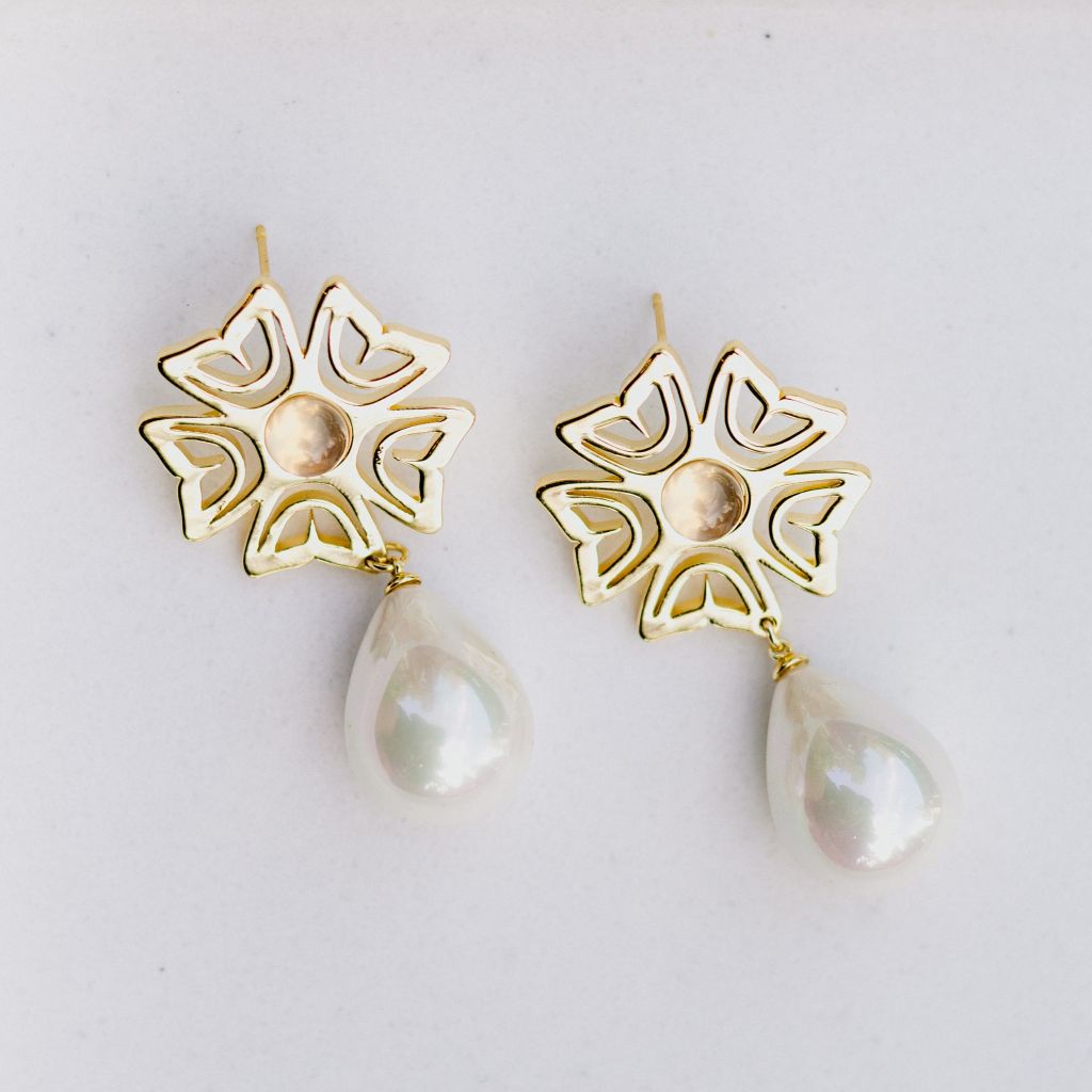 Gold floral earrings with pearl drops on a light gray background