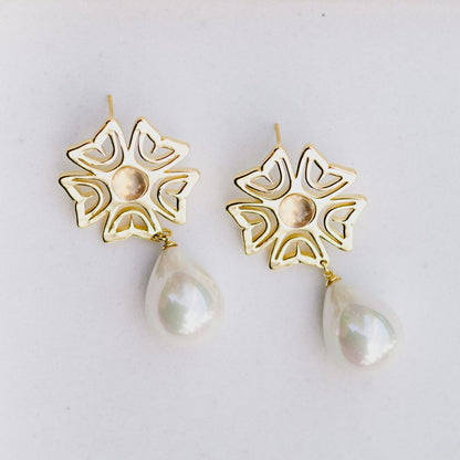 Gold floral earrings with pearl drops on a light gray background