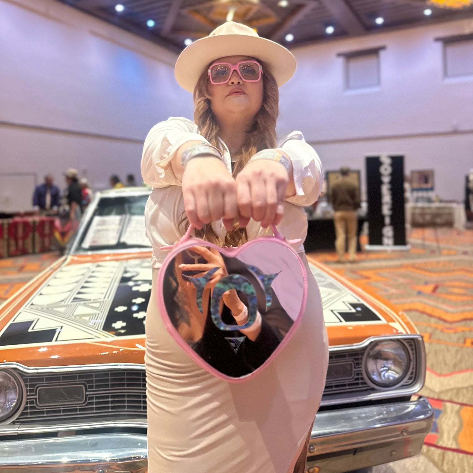 Person holding a pink heart-shaped bag with a car in the background